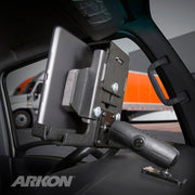 A LockVise™ Metal Locking Tablet Mount with Drill Base and Magnetic USB-C Charge Cable secures a tablet to a vehicle dashboard, with an orange and white truck outside. The word ARKON appears in the lower left corner.