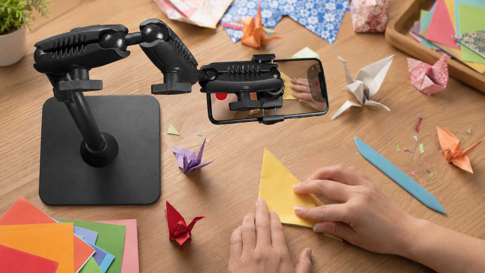 Yop down image of a content creator stand holding a phone while a pair of hands are creating some origami