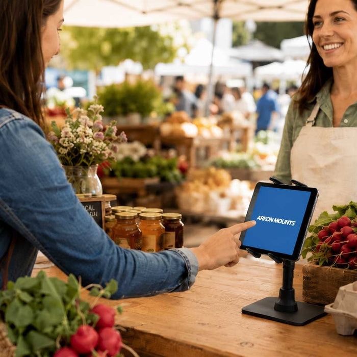 Image of two women at a farmers' market. One woman is pressing on a tablet that's on a tablet stand on the countertop. There are eggs and fress produce also on the countertop.