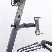 A close-up of the Slim-Grip® Tablet Holder with Forklift Front Guard Mount and 10.25 Metal Arm attached to a metal frame, gardening tools hanging below, and a white brick wall in the background.