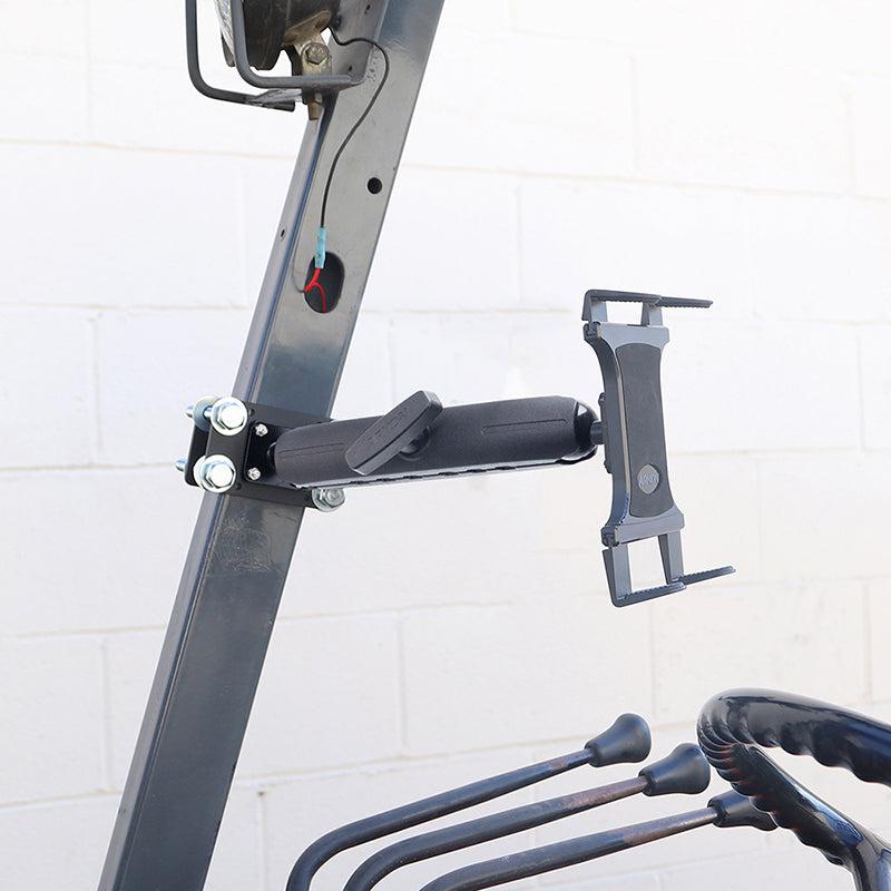 A close-up of the Slim-Grip® Tablet Holder with Forklift Front Guard Mount and 10.25 Metal Arm attached to a metal frame, gardening tools hanging below, and a white brick wall in the background.