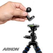 A hand holds the 1/4-20 Camera Tripod Bolt to 22mm Ball Adapter above a small black tripod adapter with flexible legs and bubble level, with the ARKON logo in the bottom left corner.