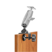 The 25mm Swivel Ball to C-Clamp Mounting Pedestal attaches to the edge of a wooden surface, features an adjustable arm with a tightening knob, and is compatible with 25mm ball mount accessories.
