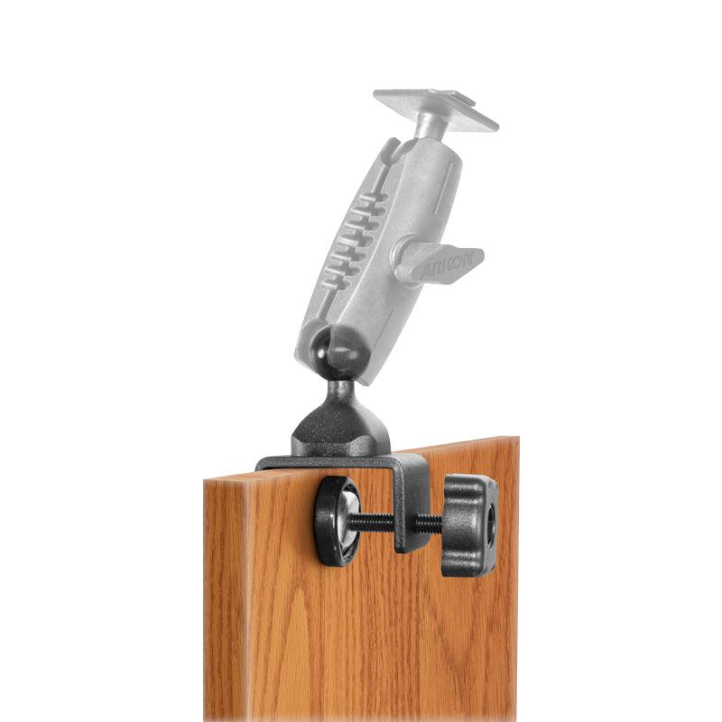 The 25mm Swivel Ball to C-Clamp Mounting Pedestal attaches to the edge of a wooden surface, features an adjustable arm with a tightening knob, and is compatible with 25mm ball mount accessories.