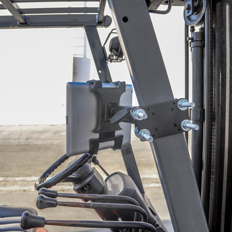 A 7 inch Robust Forklift Front Guard Slim-Grip® Tablet Mount is installed inside a forklift near the steering wheel and controls, with part of the forklift frame and outdoor pavement visible in the background.
