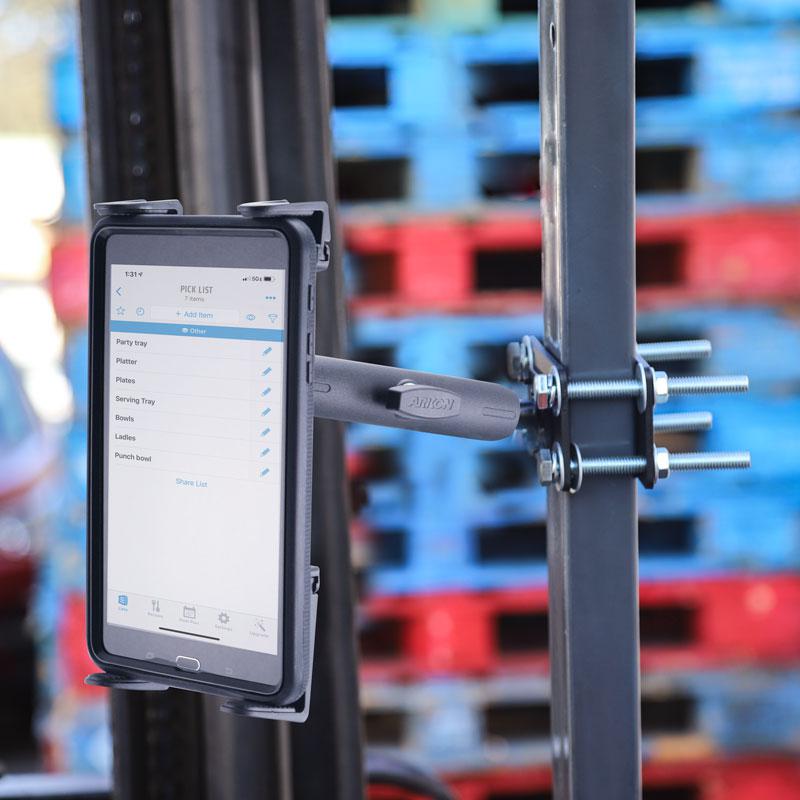 The 7.25 inch Metal Robust Forklift Front Guard Slim-Grip® Tablet Mount features an adjustable arm and metal frame secured by bolts, displaying a checklist with stacked red and blue pallets blurred in the warehouse background.