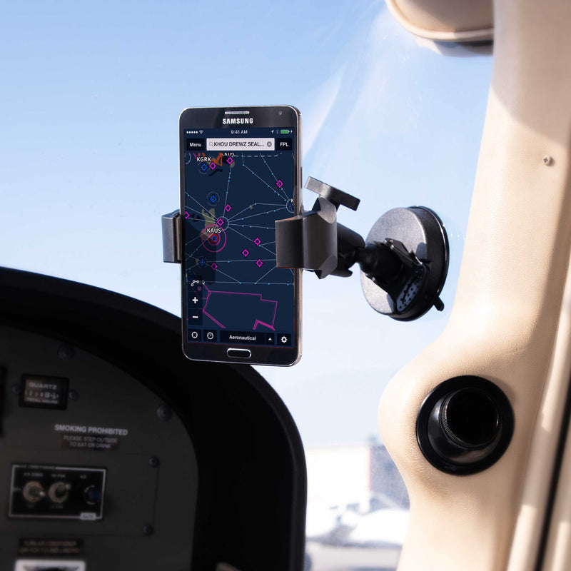 A smartphone running an aviation navigation app is held in place on an aircraft windshield by the SkyHold™ Windshield Suction Phone Mount, with cockpit instruments and a clear sky seen in the background.