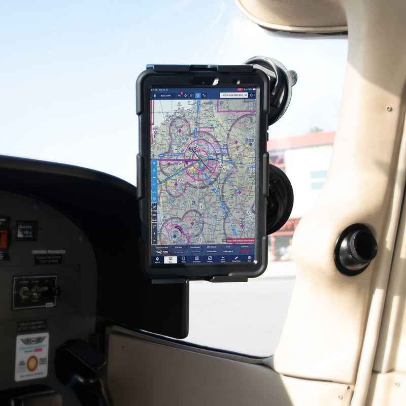 A SkyHold™ Windshield Dual Suction Tablet Mount secures a tablet showing an aviation navigation chart in the cockpit of a small aircraft, next to the control panel and window, with sunlight streaming into the interior.