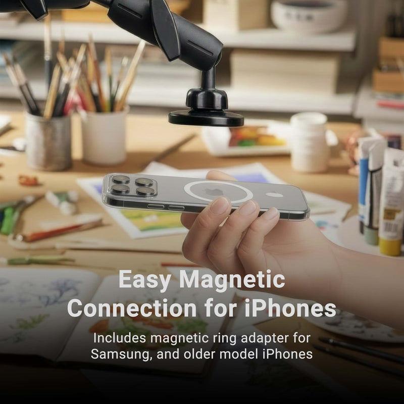 Hand holding a smartphone with a magnetic attachment device on a desk with art supplies.