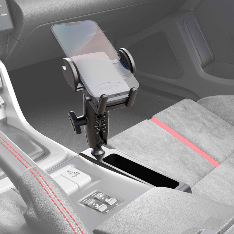 A smartphone sits in the Car Console Wedge Mega Grip™ Phone Mount Holder on the center console, beside the gear shift and cup holder. The interior features gray fabric seats accented with red stitching and trim.
