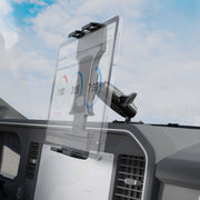 A Slim-Grip® Ultra Pro Universal Tablet Holder with Aluminum Drill-Base Mount secures a tablet on a vehicle dashboard, showing a timing app with circular timers; the windshield and cloudy sky are visible in the background.