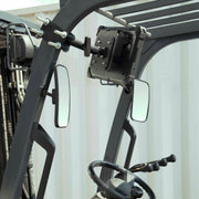 A close-up of a forklift cabin displays the steering wheel, control levers, side mirrors, and a 10.25 inch Metal Robust Forklift Front Guard VESA Mount attached to the overhead guard, with a corrugated metal wall in the background.