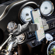 A smartphone displaying a map is secured in the RoadVise® Ultra Holder with Shaft Arm and Handlebar Mount on a motorcycle, with dashboard gauges visible in the background.