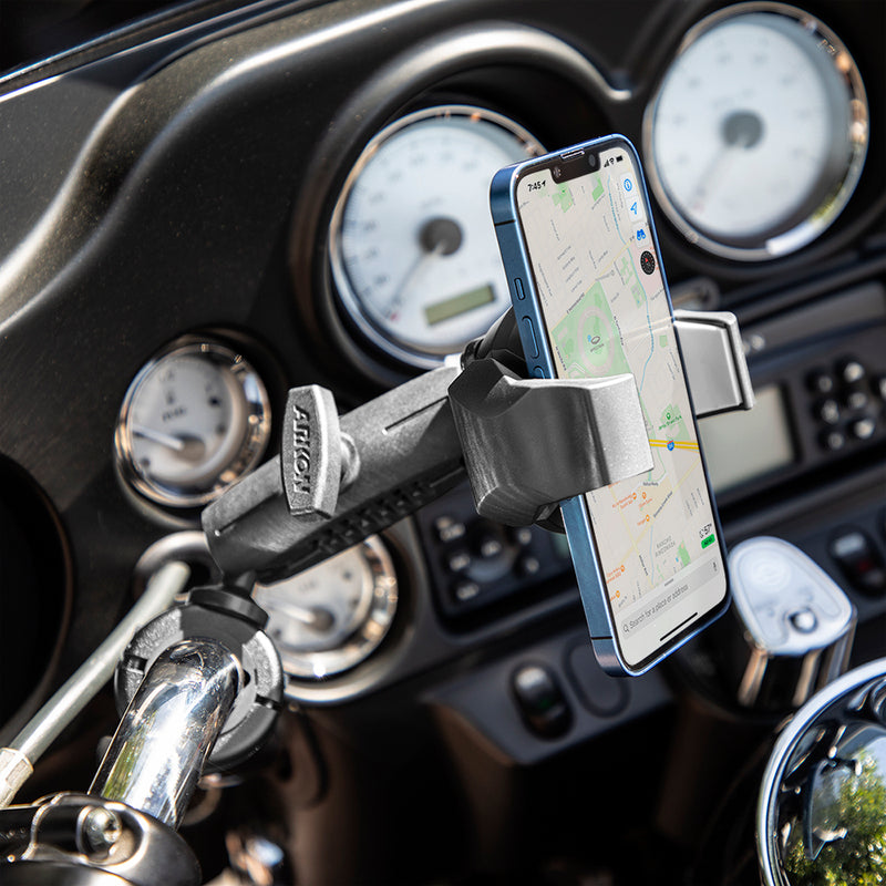 A smartphone displaying a map is secured in the RoadVise® Ultra Holder with Shaft Arm and Handlebar Mount on a motorcycle, with dashboard gauges visible in the background.