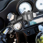Close-up of a motorcycle handlebar featuring the RoadVise® Ultra Holder with Shaft Arm and Handlebar Mount; speedometer and control gauges are visible in the background.