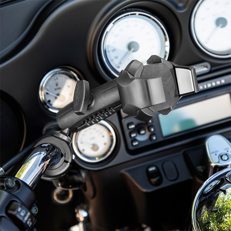 Close-up of a motorcycle handlebar featuring the RoadVise® Ultra Holder with Shaft Arm and Handlebar Mount; speedometer and control gauges are visible in the background.