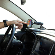 A person touches a smartphone on the Magnetic Phone Holder with Suction Mount - MagSafe Compatible, showing its home screen; the steering wheel and infotainment system are also visible.
