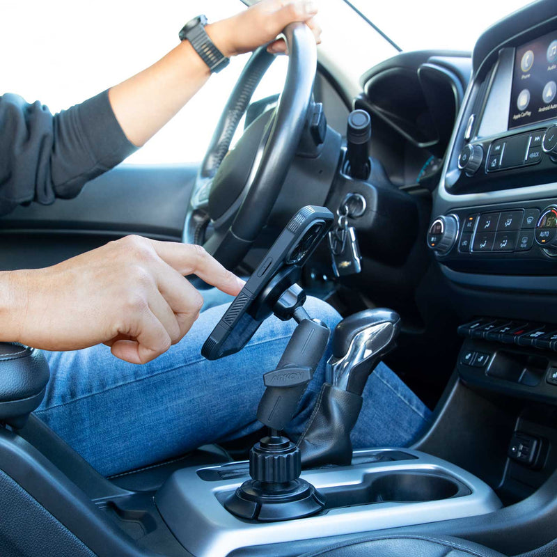 A person in a car uses a smartphone on the Magnetic Phone Holder with Car Cup Mount (MagSafe Compatible), one hand on the wheel, the other touching the screen.