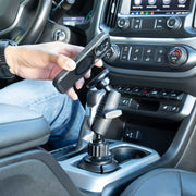 A person holds a smartphone near the Magnetic Phone Holder with Car Cup Mount - MagSafe Compatible, attached beside a car’s gear shift inside a modern vehicle, highlighting the dashboard and controls.