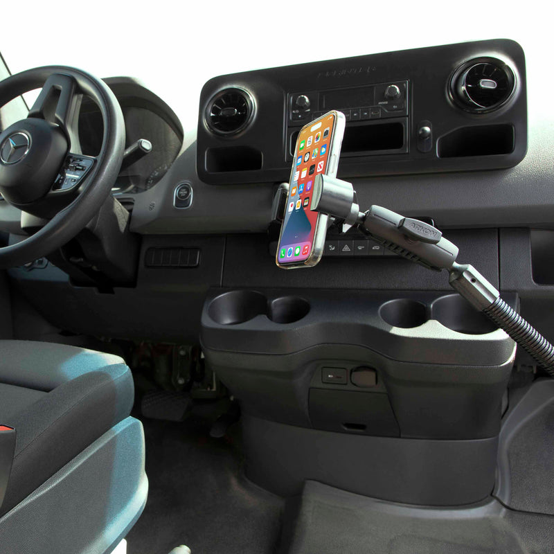 The RoadVise® Heavy-Duty Seat Rail or Floor Phone Mount holds a smartphone securely, attaching to the vehicle’s seat rail or floor near the dashboard, steering wheel, and cup holders in a modern car interior.