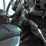 A smartphone is mounted on the RoadVise® Heavy-Duty Seat Rail or Floor Phone Mount near the driver’s seat and steering wheel, with the car’s interior and dashboard controls visible in the background.