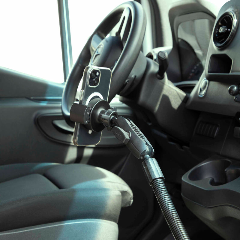 A smartphone is secured to the RoadVise® XL Heavy-Duty Seat Rail or Floor Tablet or Phone Mount near the drivers seat and steering wheel, enabling hands-free access and convenience while driving.