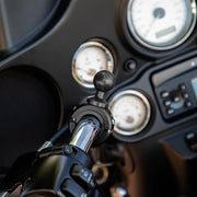 A close-up of a motorcycle handlebar shows the Aluminum Motorcycle Handlebar Mount - 25mm (1 inch) Compatible securely holding a phone or GPS, with an instrument panel and gauges visible in the background.