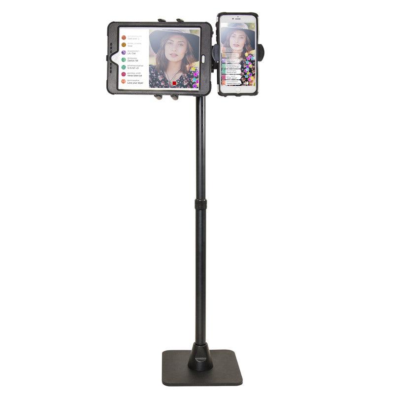 The TW Broadcaster Combo Slim-Grip® Ultra 29-inch Stand Holder securely mounts both a tablet and smartphone side by side, showing a woman in a hat live streaming with visible comments and reactions on both screens.