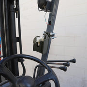 The Barcode Scanner Universal Forklift Front Guard Mount holds a barcode scanner and hand sanitizer dispenser beside the steering wheel and levers of a forklift, set against a white brick wall for efficient warehouse fulfillment.