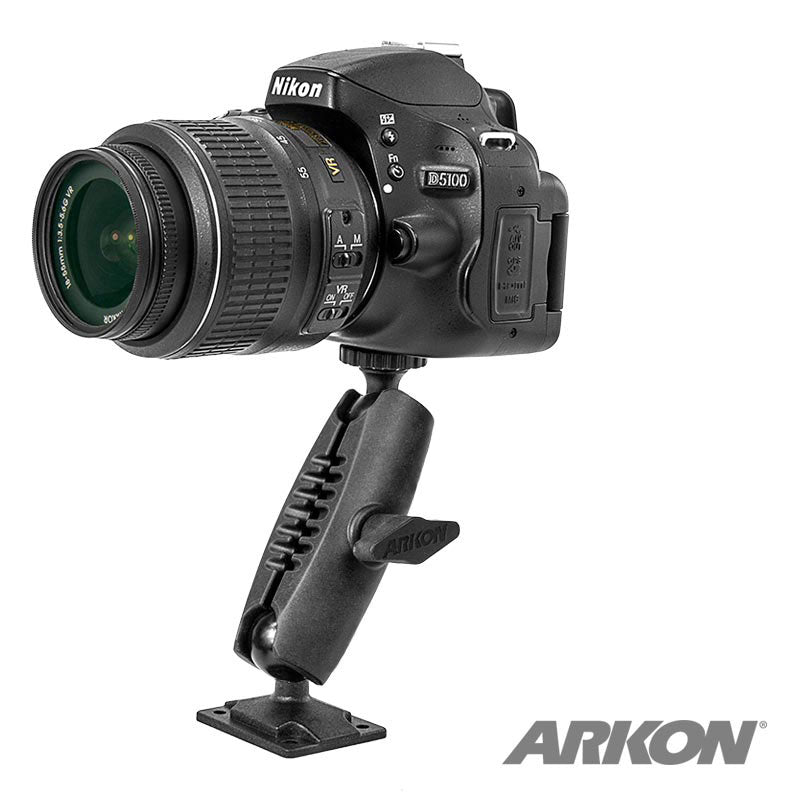 A Nikon D5100 DSLR camera is mounted on a black Camera Wall Mount for Nikon Sony Canon Fujifilm Olympus Cameras and Video Cameras with an adjustable arm and flat base. The mount displays the Arkon logo in the bottom right corner.