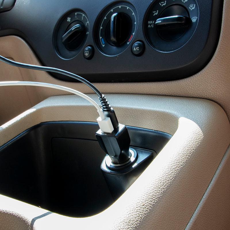 A close-up shows two charging cables plugged into the Car Charger with Quick Charge 3.0 and USB A Ports, connected to a car’s cigarette lighter socket, with the dashboard and air conditioning controls in view.