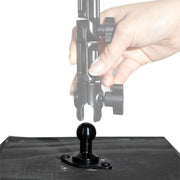 A hand adjusts a black clamp mount above a 20mm ball mount attached to a flat black surface, showing how the Arkon HD Series clamp connects to the ball joint using the Diamond 2-Hole AMPS to 20mm Ball Adapter.