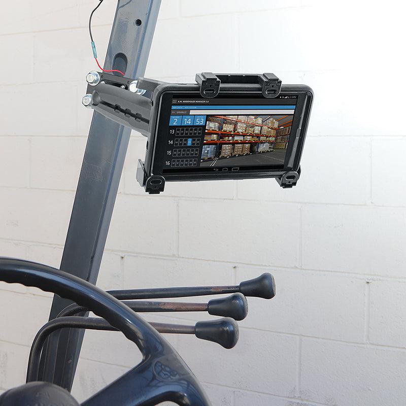A LockVise™ Locking Forklift Front Guard Tablet Mount with 10.25 inch Metal Robust™ Shaft secures a rugged tablet showing inventory and shelves, with forklift controls in front of a white brick wall background.