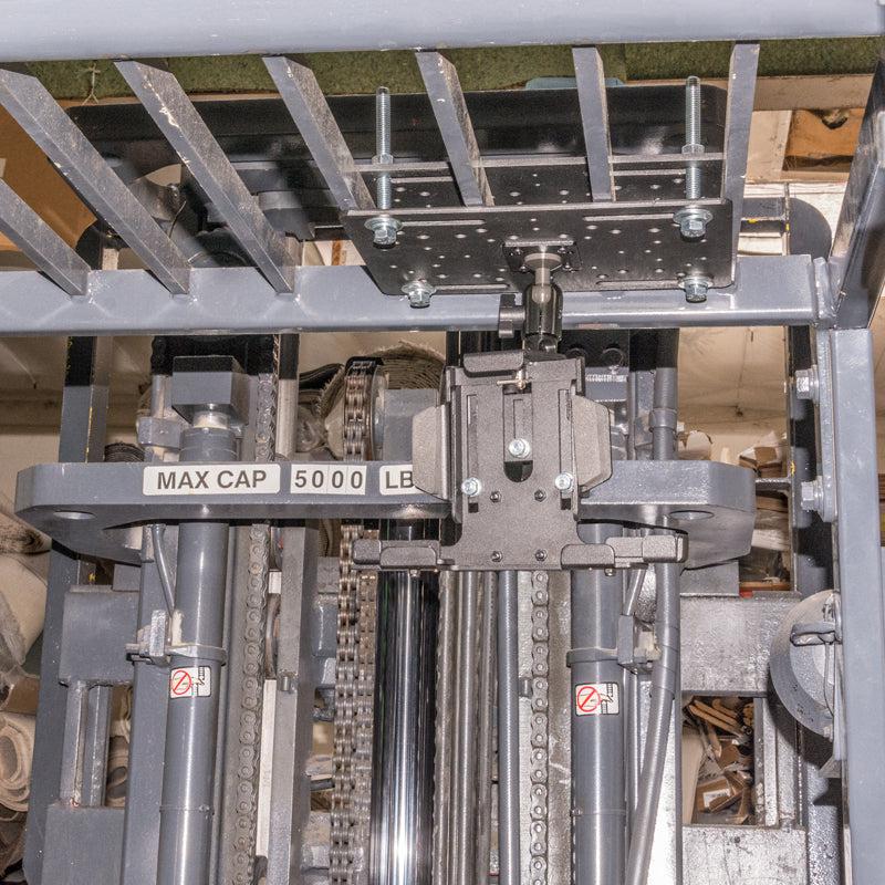 Close-up of a forklifts lifting mechanism with metal parts, chains, and a MAX CAP 5000 LB label. Warning stickers and a LockVise™ Metal Locking Overhead Guard Tablet Mount with Multi-Pivoting Arm are also visible on the machinery.