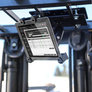 A LockVise™ Locking Forklift Overhead Guard Tablet Mount with Robust™ Adjustable Arm secures a tablet on heavy machinery displaying an inventory management app, with blurred industrial equipment and blue sky in the background.
