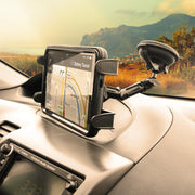 A car dashboard features a smartphone with GPS navigation, mounted using the Heavy-Duty Multi-Angle Slim-Grip® Tablet Suction Mount with 8 Arm; mountains and trees are visible through the windshield under a cloudy sky.