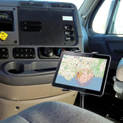 A Heavy-Duty Truck Seat Rail or Floor Slim-Grip® Tablet Mount with 22 inch Arm secures a tablet displaying a map near the drivers seat, close to the dashboard. The cab interior also features control panels, buttons, and a cupholder.