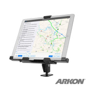 The LockVise™ Metal XL Locking Tablet Holder with Drill Base Mount in sleek black securely holds a tablet displaying map directions. ELD compliant and adjustable, it’s attached to a flat surface with the ARKON logo in the bottom right corner.