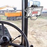 Inside a vehicle, a LockVise™ Metal Locking Tablet Mount with Drill Base Mount holds a tablet near the windshield displaying a construction site plan; outside, a yellow dump truck sits on a dirt lot.