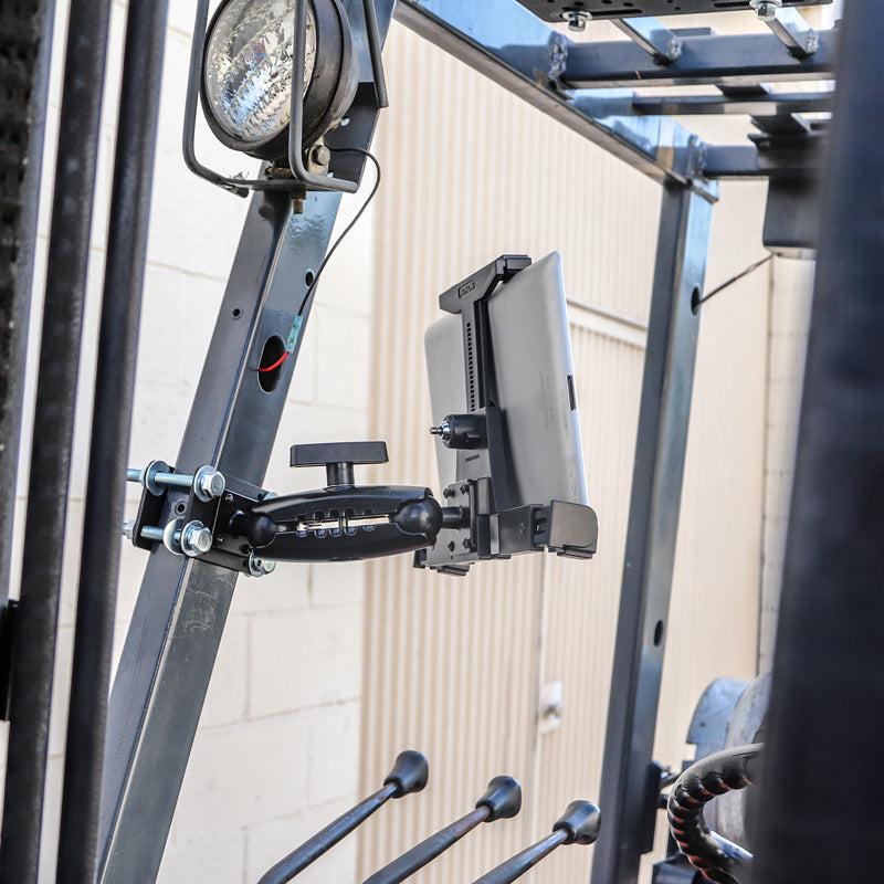 The LockVise™ Locking Forklift Front Guard Tablet Mount with 5 Robust™ Shaft is installed on a forklift’s metal frame, with nearby levers and a work light clearly visible.