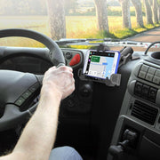 A driver uses the LockVise™ Locking Phone Mount with 2.75 Arm and Metal AMPS Drill Base, securing their smartphone to the dashboard for navigation, with trees and the road visible through the windshield.