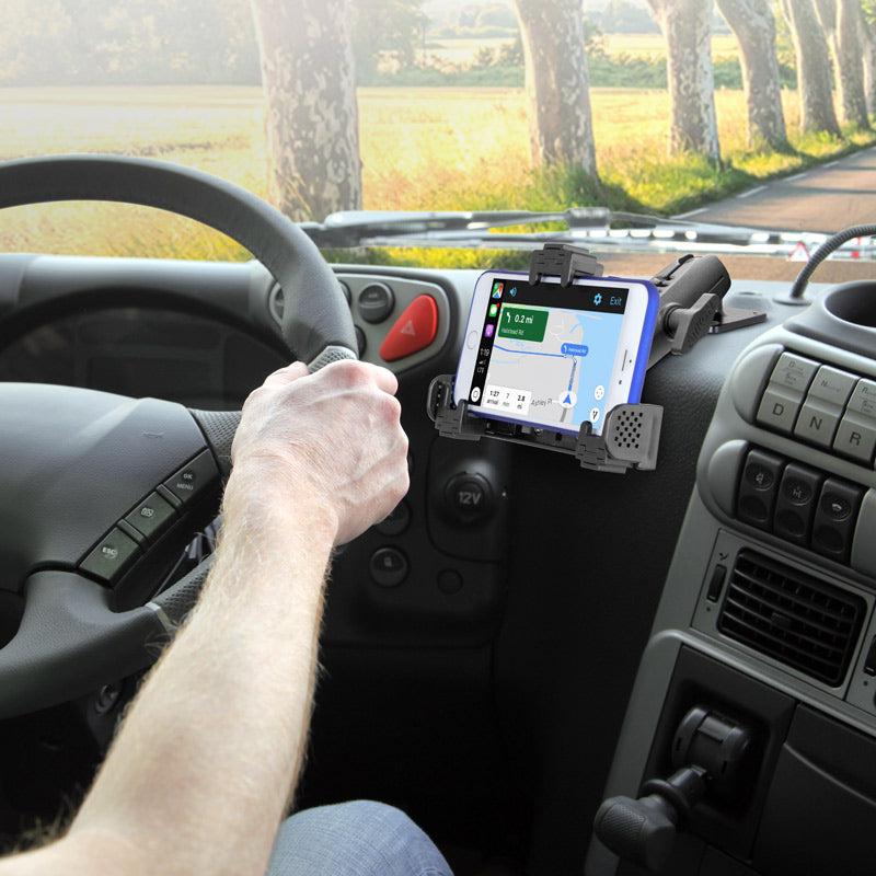 A driver uses the LockVise™ Locking Phone Mount with 2.75 Arm and Metal AMPS Drill Base, securing their smartphone to the dashboard for navigation, with trees and the road visible through the windshield.