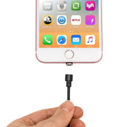 A hand holds a Magnetic USB to Lightning Charge Cable in black, ready to attach it to a smartphone’s charging port while app icons are visible on the screen.