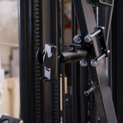 Close-up of the Mega Grip™ Forklift Front Guard Mount securely fastened to a metal frame with bolts and screws, set against blurred industrial equipment in a warehouse.