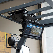 The LockVise™ Metal Locking Forklift Overhead Guard Tablet Mount with 5 Metal Robust™ Shaft securely holds a tablet showing warehouse management on a forklift’s overhead guard, with cardboard boxes in the background.