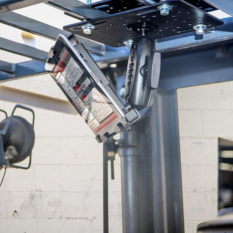 A rugged tablet is mounted outdoors near a beige brick wall using the LockVise™ Metal Locking Forklift Overhead Guard Tablet Mount with a 5 Metal Robust™ Shaft.