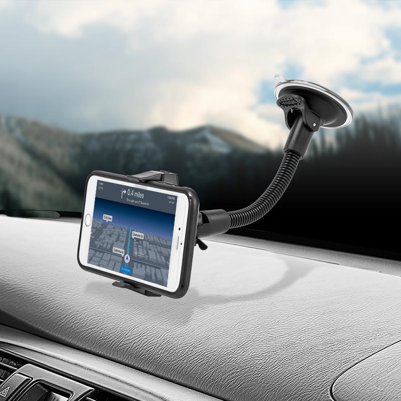 An iPhone is mounted on the Mobile Grip 2 Windshield Suction Car Mount with an 8.5 arm, showing a navigation map. The universal mount attaches to the dashboard, and snowy mountains are visible through the windshield.