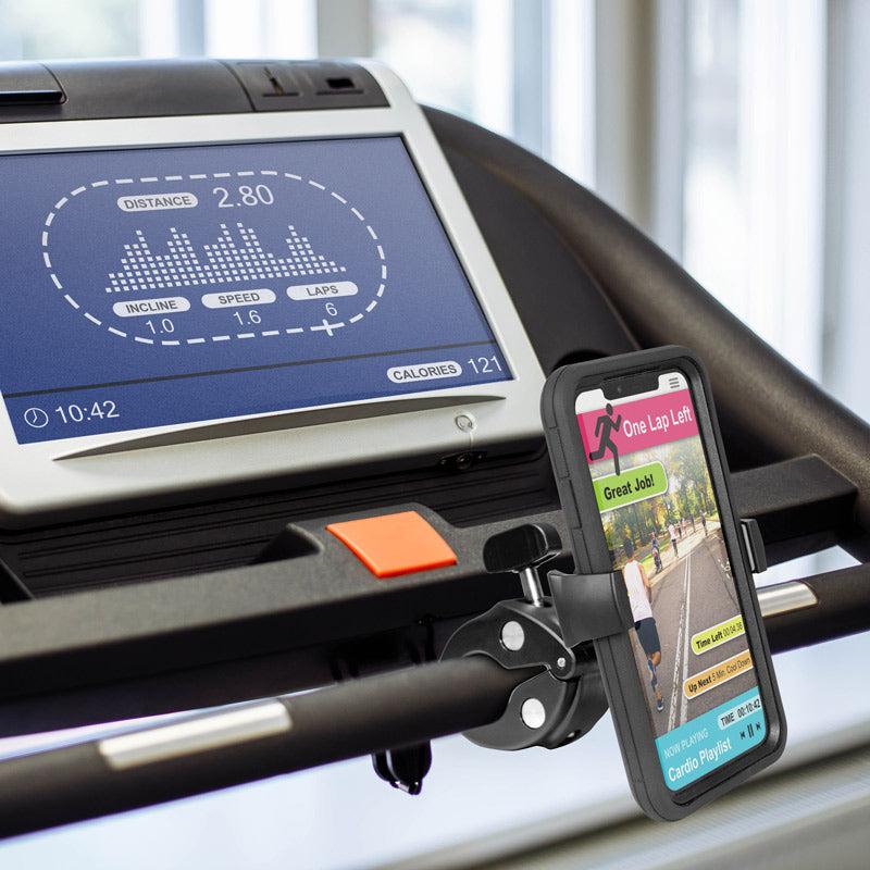 A treadmill display shows workout stats, while a smartphone held by the Mobile Grip 5 Phone Holder with Clamp Mount displays motivational app messages. Both devices are attached to the exercise equipment’s console.