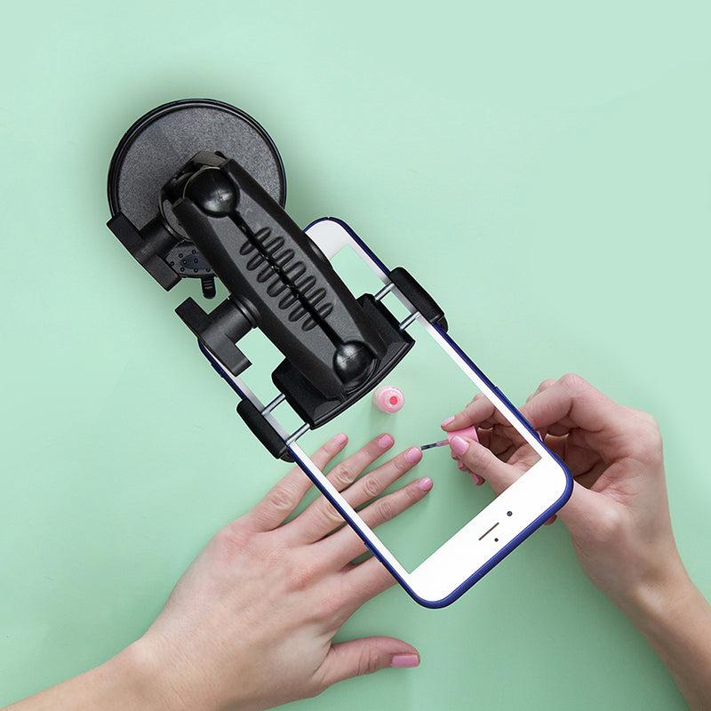 The Mobile Grip 5 Robust Phone Mount Holder for iPhone, Galaxy, and Note secures a phone above someone painting their nails pink, recording a close-up of the manicure on a light green background.