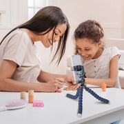 A woman and a young girl smile while painting nails at a table, recorded by the Mobile Grip 5 Tripod Phone Mount for iPhone, Galaxy, and Note—a perfect accessory for content creators. Nail polish bottles and beauty items fill the white table.